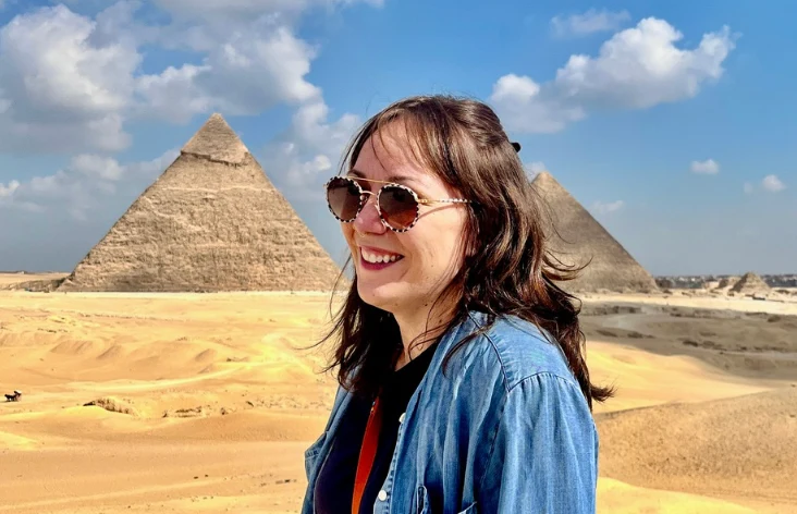 Laura in front of the Great Pyramid in Cairo, in a denim shirt and tortoise sunglasses, sun on the dunes.